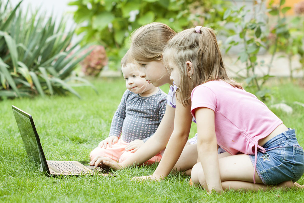 Children using laptop in the meadow